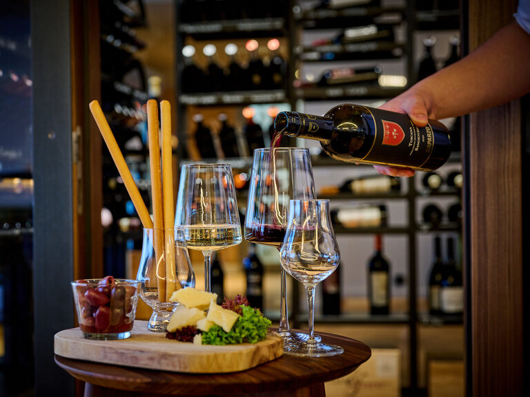 Käse, Oliven & Grissini - daneben Weingläser, in die gerade eingeschenkt wird, vor dem begehbaren Weinschrank des Restaurant ASAM. Käse, Oliven & Grissini - daneben Weingläser, in die gerade eingeschenkt wird, vor dem begehbaren Weinschrank des Restaurant ASAM.