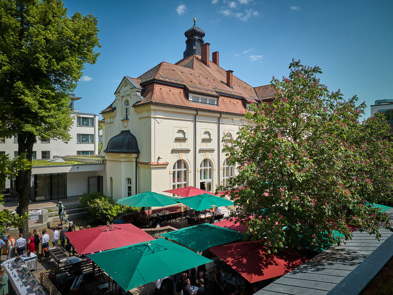 Biergarten des Hotel & Restaurant ASAM in Straubing mit Sonnenschirmen und Blick auf das historische Offizierskasino.