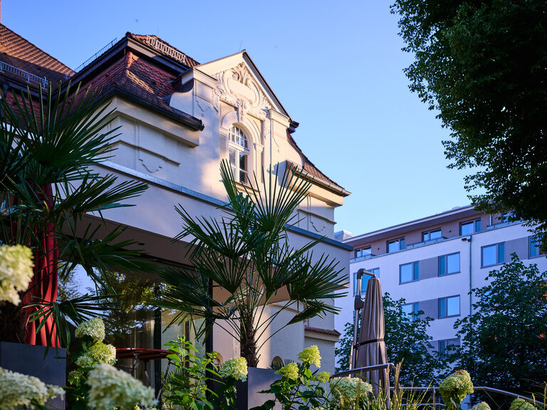 Historische Fassade des Offizierskasinos im Hotel ASAM in Straubing, von der Terrasse aus mit sommerlicher Bepflanzung.