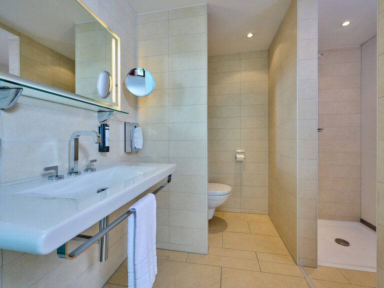 Modernes, helles Badezimmer im 4-Sterne-S-Hotel ASAM Straubing mit Waschbecken, WC und Dusche.