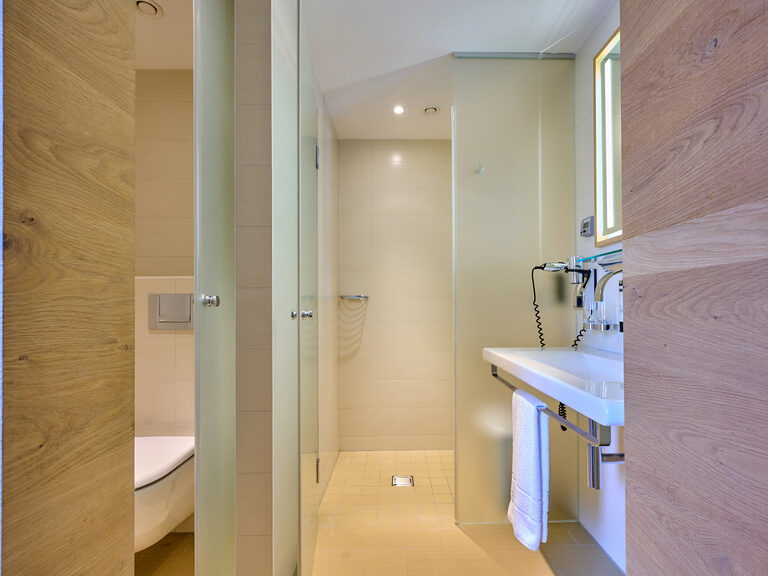 Helles Bad mit Milchglastüren, WC, Dusche und Waschbecken im Businesshotel Asam Straubing.