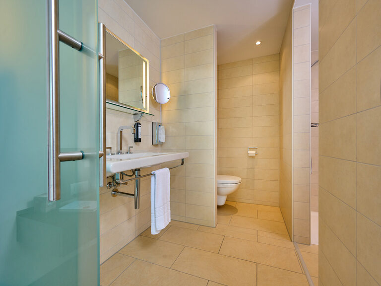 Helles, einladendes Bad im 4-Sterne-S Hotel Asam Straubing mit Waschbecken, WC und Dusche.
