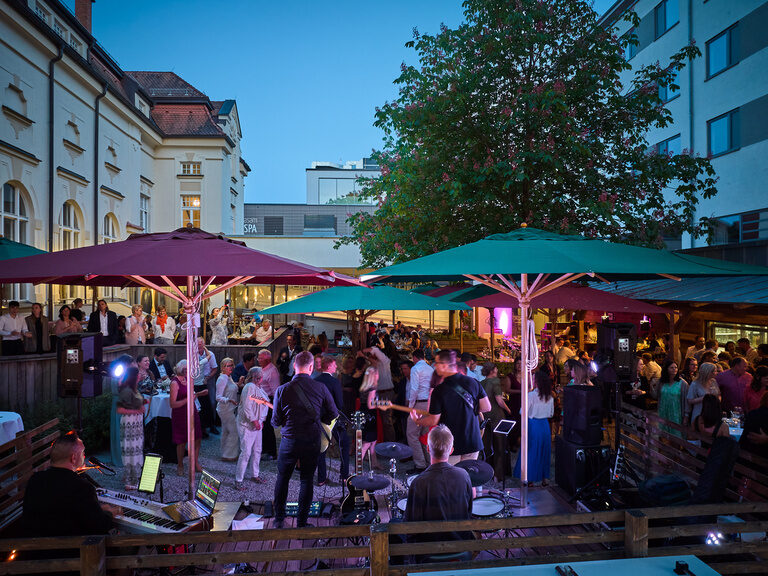 Abendlicher Blick in den Biergarten des Hotel & Restaurant ASAM in Straubing mit vielen feiernden Gästen.