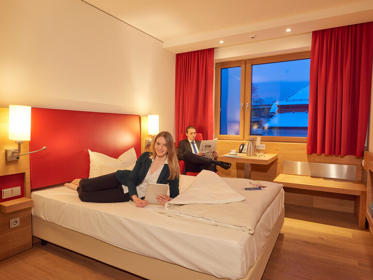 Businesszimmer mit Queensize-Bett im 4-Sterne-S Hotel Asam Straubing, zwei Gäste im Zimmer. Businesszimmer mit Queensize-Bett im 4-Sterne-S Hotel Asam Straubing, zwei Gäste im Zimmer.