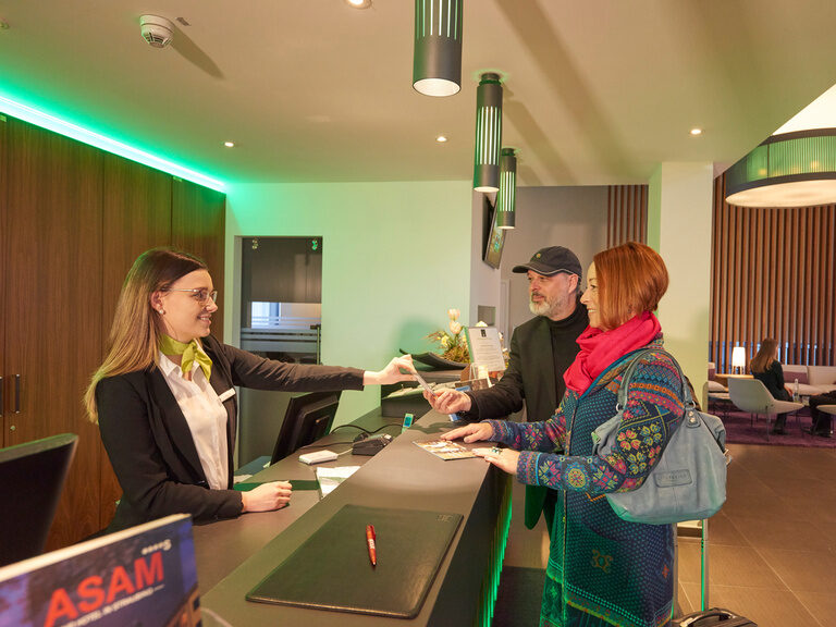 Gäste beim Einchecken an der Rezeption in der modernen Lobby des 4-Sterne-S Hotel Asam Straubing.