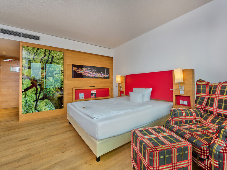 Comfort Doppelzimmer im Businesshotel ASAM in Straubing mit Parkettboden, gemütlichem Sessel und warmen Farben.