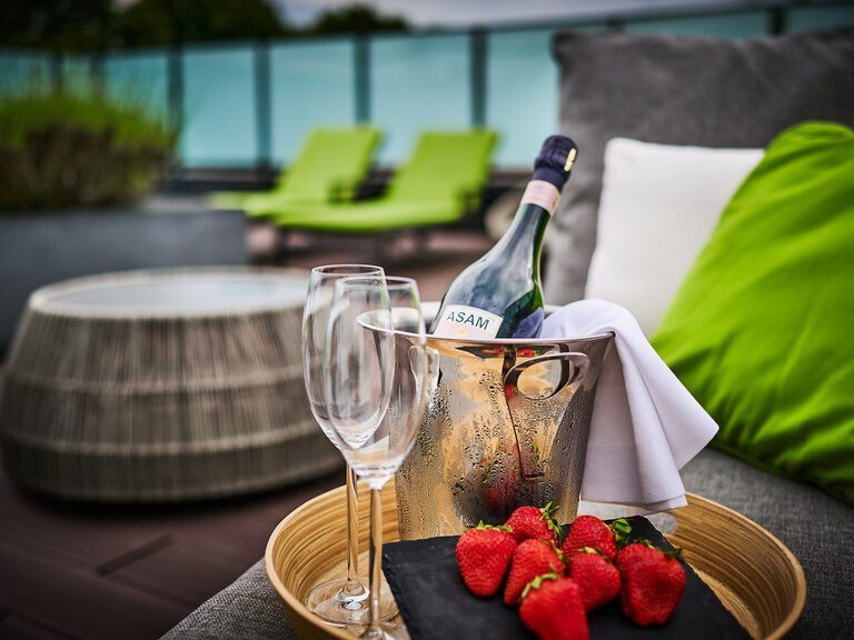 Detailaufnahme von Sekt, zwei Gläsern und Erdbeeren auf der begrünten Dachterrasse im sommerlichen Wellnessbereich des Hotel ASAM.