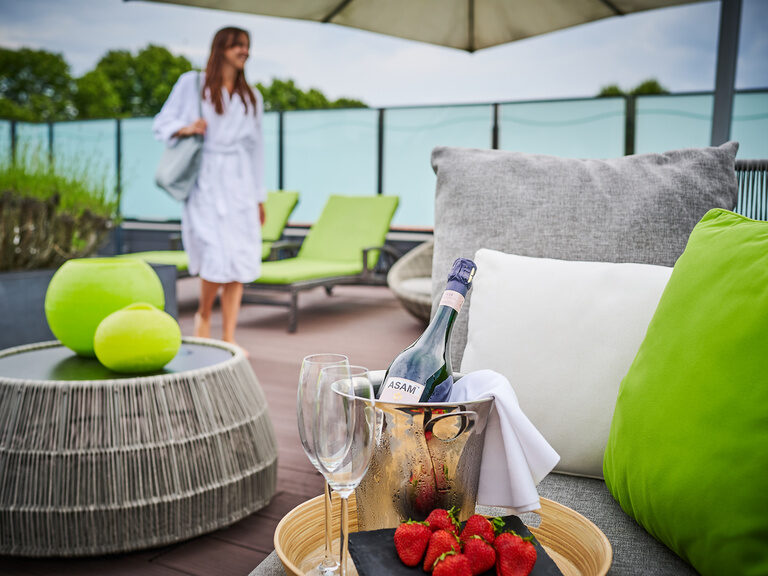 Eine Frau in einem weißen Bademantel steht auf der Terrasse des Hotel ASAM und genießt den Ausblick.