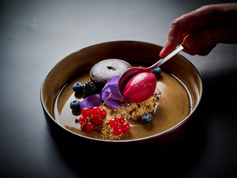 Rotes Sorbet wird gerade auf einem eleganten Dessert-Teller mit Schokoküchlein angerichtet. Rotes Sorbet wird gerade auf einem eleganten Dessert-Teller mit Schokoküchlein angerichtet.