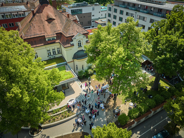 Luftaufnahme des grünen Biergartens am historischen Offizierskasino im Hotel ASAM in Straubing mit feiernder Gesellschaft.