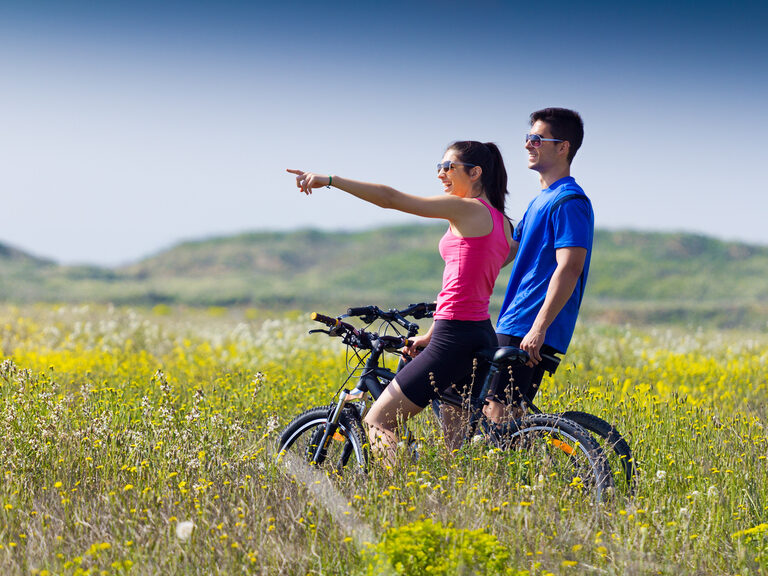 Junges, sportliches Pärchen auf Fahrrädern bei einem Halt auf einer grünen Wiese.