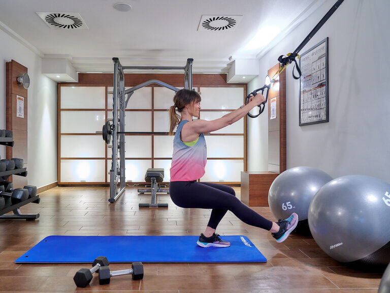 TRX-Training im Fitnessraum des Hotels Asam Straubing: Frau nutzt Suspension Band für Ganzkörper-Workout.