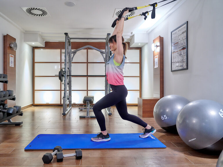 Frau trainiert mit TRX Suspension Band im Fitnessraum des 4-Sterne-S Hotel Asam Straubing.