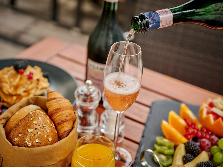 Ein Glas Sekt wird auf einem reich gedeckten Frühstückstisch eingeschenkt. Ein Glas Sekt wird auf einem reich gedeckten Frühstückstisch eingeschenkt.