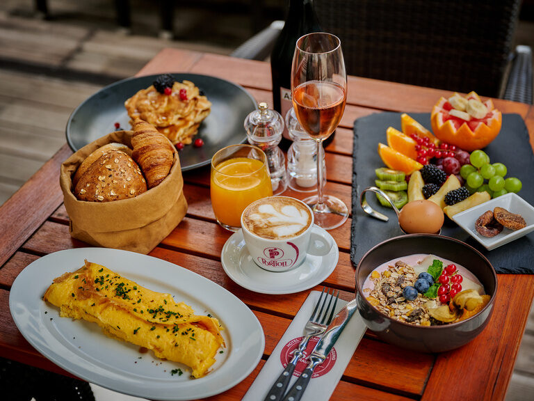 Reich gedeckter Frühstückstisch mit Speisen vom Buffet: Müsli, Obst, Eierspeisen, Backwaren, Kaffee, Saft und vieles mehr.