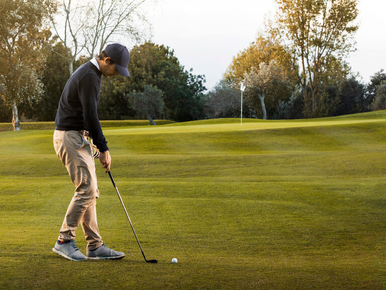 Ein Golfer beim Abschlag auf einem grünen Golfplatz, umgeben von Bäumen.