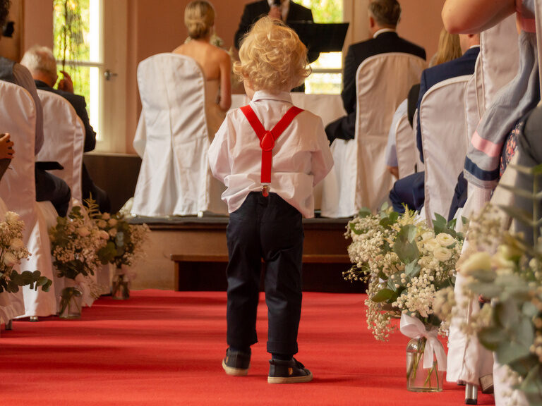 Kleines Kind auf dem roten Teppich zwischen Stühlen mit weißen Hussen bei einer Hochzeit im Hotel ASAM.