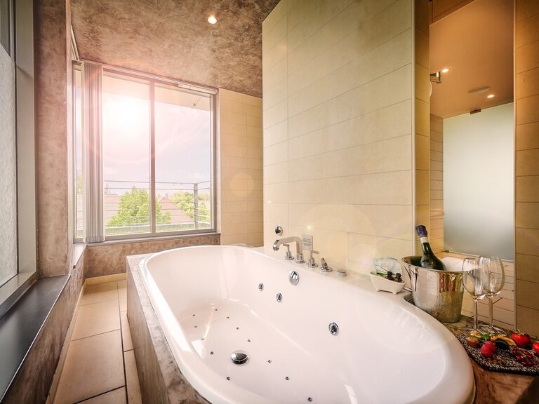 Whirlpool-Badewanne in hellem Bad mit Fensterfront und Blick auf die Stadt Straubing in einer Suite des Hotel ASAM.