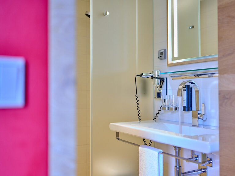 Nahaufnahme Waschbecken mit Föhn und Pflegeprodukten in hellem Bad im 4-Sterne-S Hotel Asam Straubing.