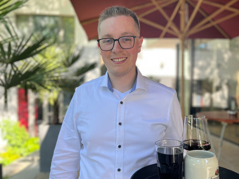 Servicemitarbeiter im Hotel & Restaurant ASAM in Straubing mit Tablett in der Hand.