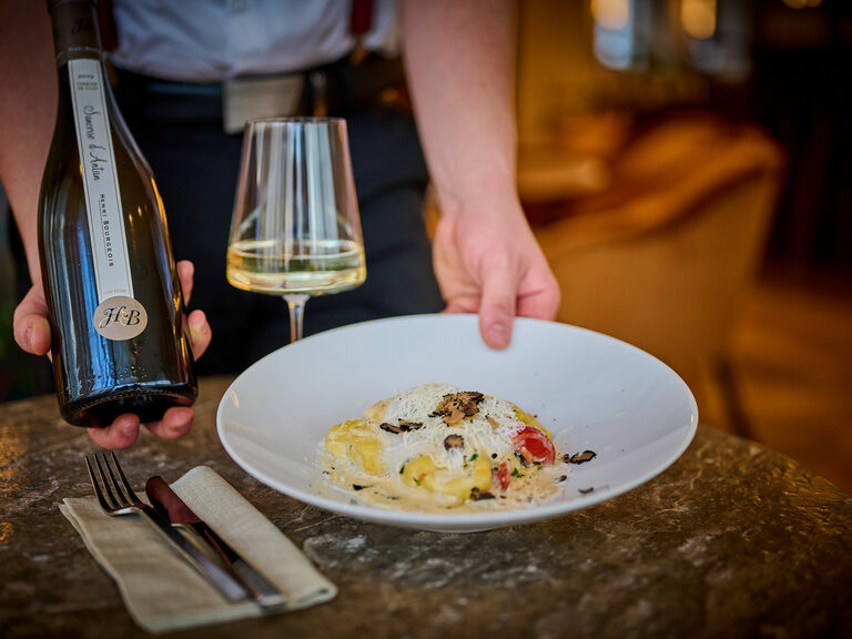 Ein Teller Pasta mit Trüffel und ein Weißwein werden an einem Tisch im Restaurant ASAM serviert. Ein Teller Pasta mit Trüffel und ein Weißwein werden an einem Tisch im Restaurant ASAM serviert.