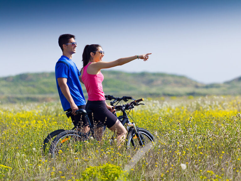 Ein junges Paar auf Fahrrädern bei einem Stopp auf einer Wiese.