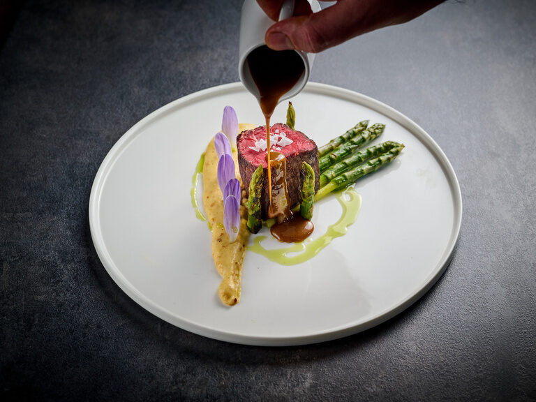 Sauce wird auf einen edel angerichteten Teller mit Rindfleisch und Beilagen gegossen.