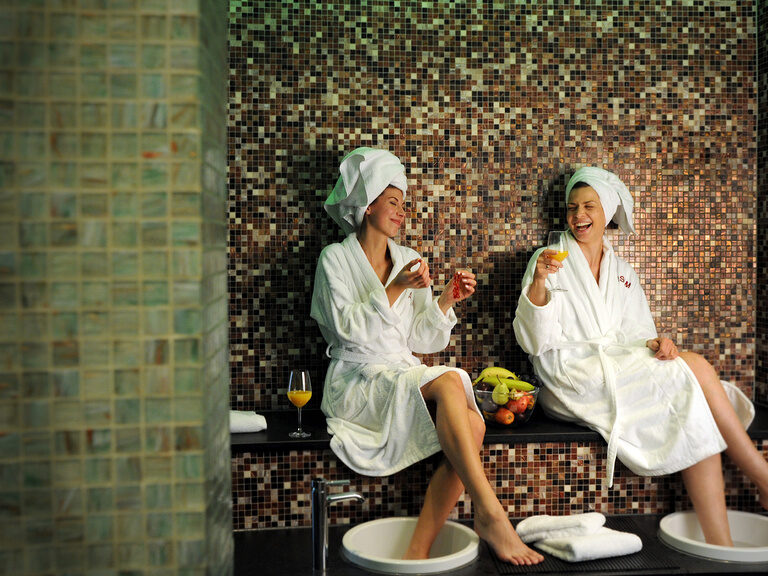 Zwei Frauen sitzen lachend mit Handtüchern und Bademantel im Wellnessbereichd es 4-Sterne-S-Hotel ASAM in Straubing. Zwei Frauen sitzen lachend mit Handtüchern und Bademantel im Wellnessbereichd es 4-Sterne-S-Hotel ASAM in Straubing.