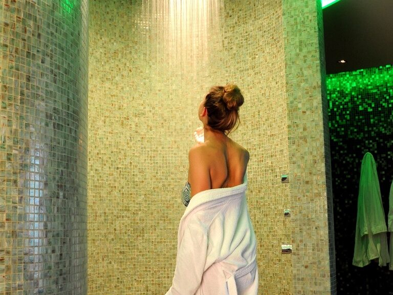 Eine Frau mit Bademantel vor der Regenbogendusche im Wellnessbereich des 4-Sterne-S Hotel ASAM in Straubing, Niederbayern.